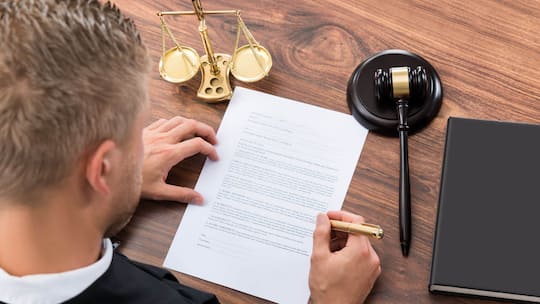 Ein Mann füllt ein Formular aus, das neben einem Richterhammer und einer Waagschale für Gerechtigkeit liegt. In welchen Fällen lohnt es sich, Einsprache gegen einen Strafbefehl zu erheben?