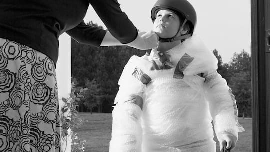 Ein Kind in eine Schutzhülle gepackt und einem Helm auf dem Kopf.