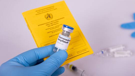 Eine medizinische Person hält einen Papier-Impfausweis und den Impfstoff in der Hand.