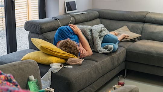 Ein Mann liegt krank auf dem Sofa.