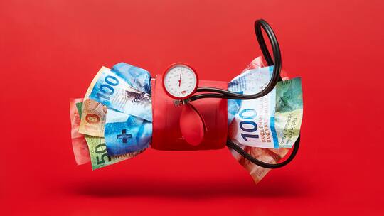 Bild zum Thema Gesundheitskosten.Ein Blutdruckmessgeraet zerquetscht Schweizer Banknoten der 9. Banknotenserie. Fotografiert am Freitag, 29.09.23 im Studio in ZürichFoto: Yves Roth