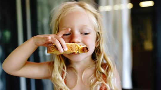 Mädchen beisst in Zmorgebrot - Haferflocken statt Cornflakes, Hüttenkäse statt Nutella: Wie kleine Änderungen beim Frühstück die Schulleistung beeinflussen – und welche Lebensmittel Ihr Kind wach halten
