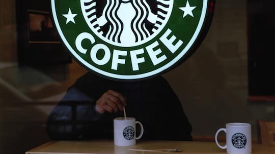 A man stirs his coffee from behind a Starbucks sign in London.