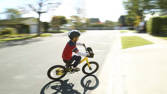 Ein kleines Kind fährt mit einem Kindervelo auf einer ruhigen Nebenstrasse.