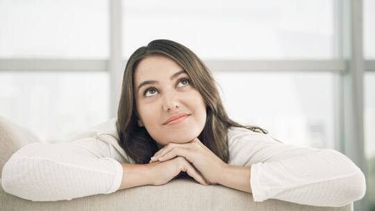 Eine junge Frau hat die Hände übereinander gelegt und blickt träumerisch nach oben.