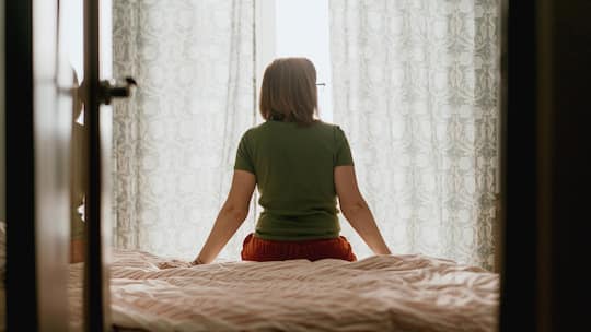 Frau sitzt auf Bett, schaut aus dem Fenster - Eine Frau hat sich fast zwei Jahrzehnte um Haus und Kinder gekümmert. Unterhalt bekommt sie nach der Scheidung aber nur sechs Monate lang