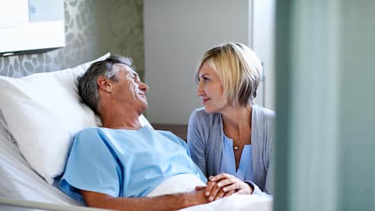 Mann im Spitalbett, Frau hält seine Hand - Wer ohne Ehevertrag zusammenlebt, wiegt sich oft in falscher Sicherheit. Von der AHV gibt es im Todesfall keinen Rappen – und bei der IV drohen zermürbende Kämpfe um jeden Franken