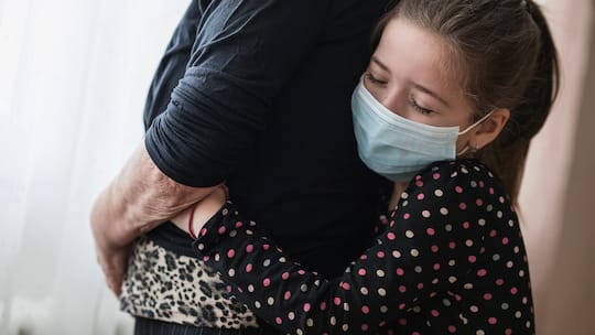 Kind mit Maske umarmt ältere Person