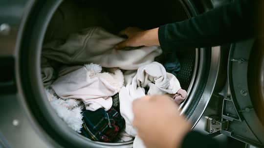 Young caucasian woman hands putting her dirty clothes in the washing machine in a laundromat. Self service laundry