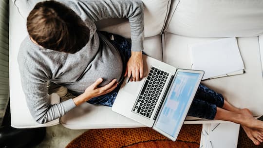 An aerial view of a pregnant woman sitting on her couch using her laptop, working from home during the day.
1180387560