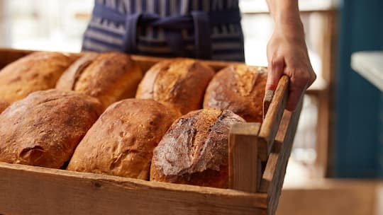 Sales Assistant In Bakery With Tray Of Freshly Baked Organic Sourdough Bread Loaves