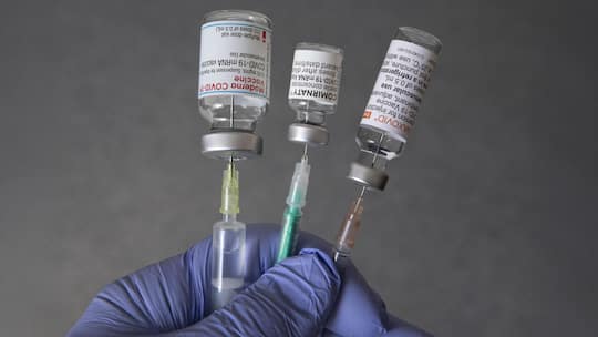 BONN, GERMANY - APRIL 27: In this illustration photo, taken in a Bonn vaccination center, shows a doctor's hand with medical syringes and the original vaccination vials from Moderna, Comirnaty (Pfizer/BioNTech) and Nuvaxovid (Novavax) on April 27, 20…