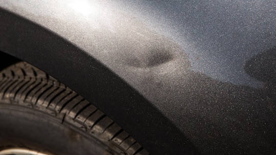 Minor car dent on car fender. Depreciation concept of dented fender for autobody repair, car maintenance, fender bender, or buying a used car or SUV with minor damage. Car exterior photographed during day, outdoors. Part of a series.