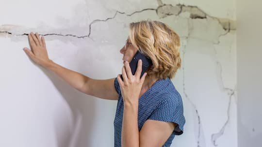 Eine Frau begutachtet die Schäden und Risse in der Hausmauer und meldet diese telefonisch der Versicherung. Wenn in der Schweiz die Erde bebt, stellt sich die Frage, welche Versicherung kommt für allfällige Schäden auf. So gestaltet sich die Situation in den Kantonen.