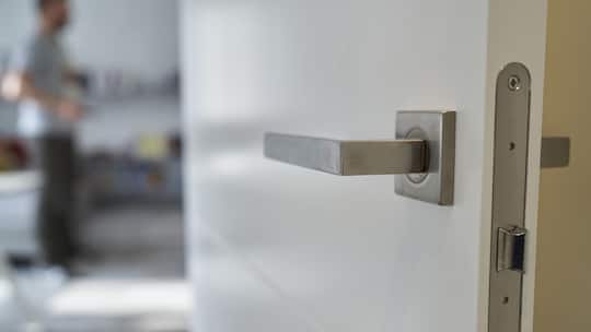Close-up of front view of modern metal entrance door handle to living room against standing unrecognizable man