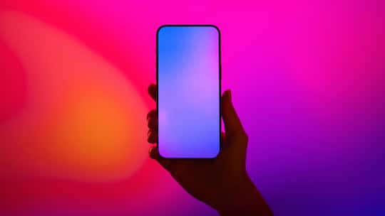 Close-up shot of a female hand holding smartphone with blank screen against illuminated LED digital display screen. Mockup image. Connecting to the future. Futuristic. Artificial intelligence. Innovation and technology concept2203621915