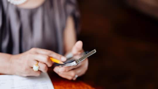Cropped shot of Asian senior woman calculating financial bills and receipts, managing personal banking and finance with smart phone in living room at home. Retirement lifestyle. Elderly and technology. Managing taxes and financial bills. Wealth manag…