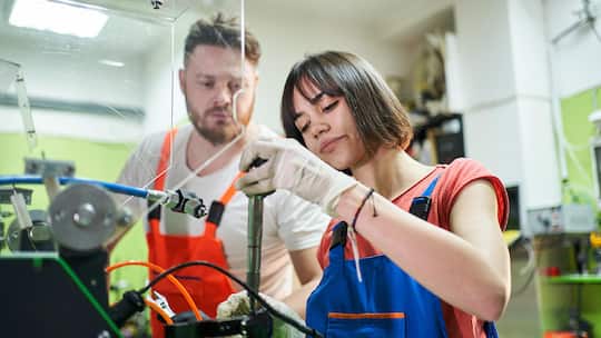 Young male mechanic and teenage female mechanic working with tools in the storage room of an auto repair shop, side view