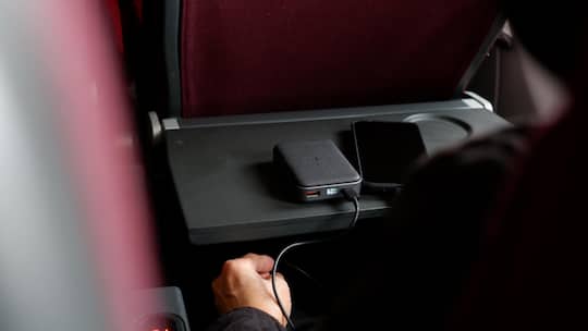Ein Fluggast lädt in einem Flugzeug sein Smartphone mithilfe einer Powerbank auf.