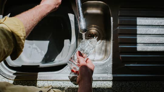A man pours water down a drain, from a transparent drinking glass, in a kitchen sink.
Original File-ID: 1509888816