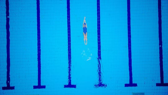 Female swimmer on evening training on swimming pool, warming up, swimming backstroke during training.