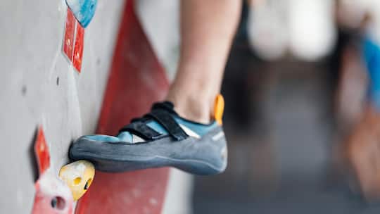 Detail of a climber's shoe firmly placed on a hold on an indoor climbing wall, showcasing grip and technique in a sport environment.