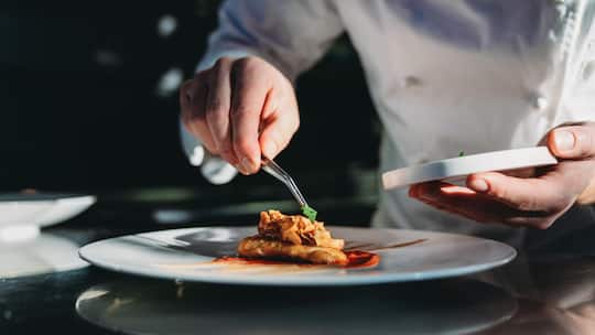 A chef is finishing the preparation of the plate. He's decorating the plate just before the serving.
