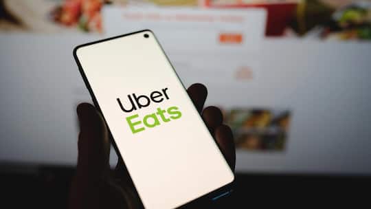 Man holding a smartphone with Uber Eats logo in front of the official website. Popular food delivery service on dark blurred backgroundHand with Uber Eats app icon on smartphone