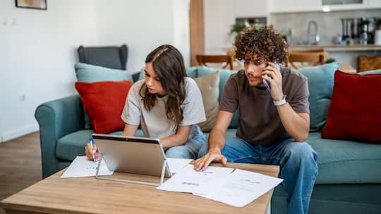 Young couple sitting on a couch, reviewing domestic budget documents and financial paperwork at home
2242837193