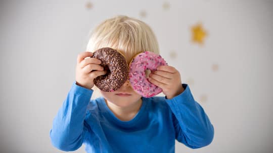 Kind hält Donuts vor die Augen - Werbung für besonders süsse, salzige und fettige Produkte an Kinder soll ab 2027 eingeschränkt werden. Noch ist die Regelung aber nicht unter Dach