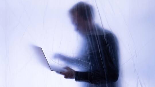 2J21B82 Silhoutte eines Büroangestellten steht hinter Plastikfolie mit Laptop