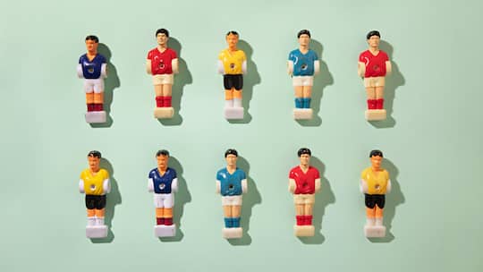 Fussball-Figuren verschiedener Nationen auf einer hellgrünen Oberfläche - Eine Firma organisiert ein Tippspiel, bei dem alle 200 Angestellten mitmachen können. Einsatz: 20 Franken. Ist das erlaubt?