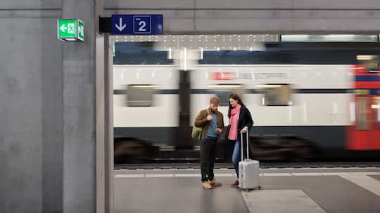Reisende warten auf den Zug an einem Schweizer Bahnhof