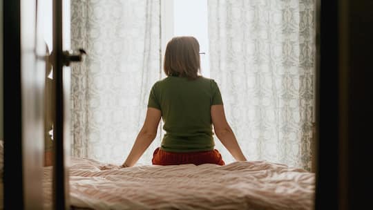 Frau sitzt auf einem Bett und schaut aus dem Fenster - Eine Frau hat sich fast zwei Jahrzehnte um Haus und Kinder gekümmert. Unterhalt bekommt sie nach der Scheidung aber nur sechs Monate lang