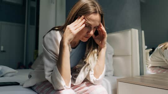 Eine Frau mittleren Alters sitzt zu Hause und h‰lt sich die H‰nde an die Schl‰fen. Kopfschmerzen, Frauengesundheit, Hormonspiegel. Finanzkrise. A middle-aged woman sitting at home holds her hands on her temples. Headache, women s health, hormon…
