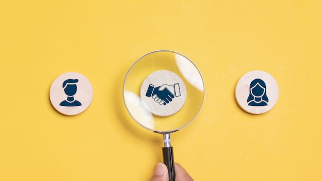 Wie sich Konflikte fair lösen lassen Drei Holzmünzen mit einem Mann, einer Frau und einem Handschlag, über dem eine Lupe liegt. Wie Mediation funktioniert.