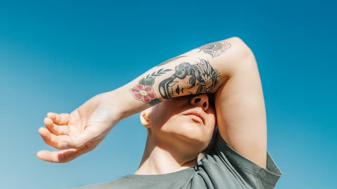 Weg mit dem Tattoo – bloss wie? Frau hält sich tätowierten Arm vors Gesicht - Nicht jede Tätowierung passt ein Leben lang. Doch die Zeichnung weglasern zu lassen, ist nicht nur teuer und langwierig – es ist auch mit Risiken verbunden