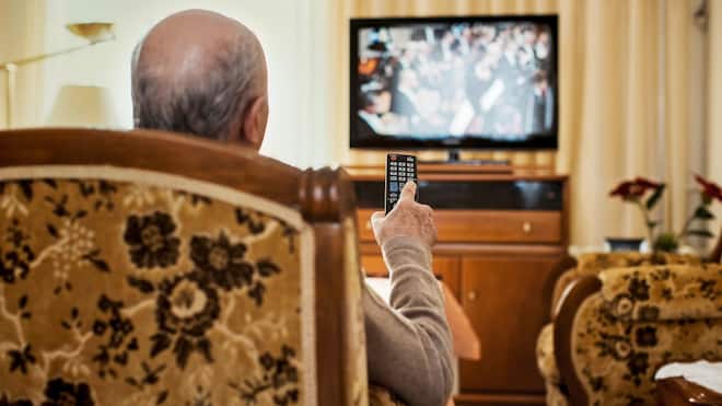 Im Heim und trotzdem TV-Gebühren zahlen? Ein älterer Herr sitzt in einem Sessel und bedient mit der Fernbedienung ein TV-Gerät.