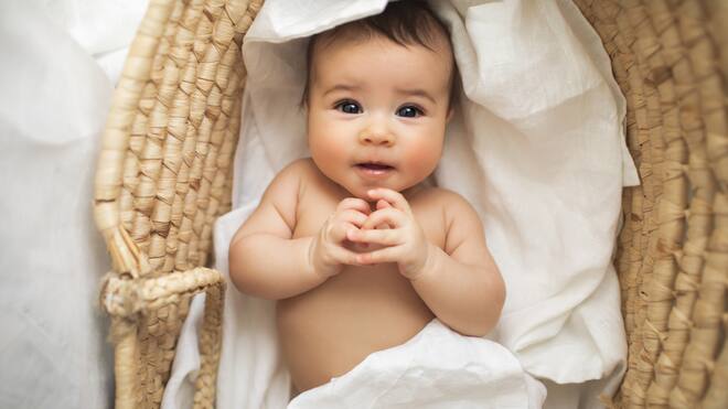 Samenspende für Singles? Was jetzt gilt und was sich bald ändert Ein kleines Baby liegt umwickelt in weissen Laken in einem Korb und lächelt süss in die Kamera.