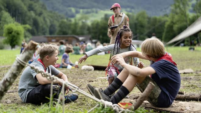 «Wir treffen den Zeitgeist» Zwei Pfadfinder und eine Pfadfinderin sitzen auf einer Wiese, reden und lachen