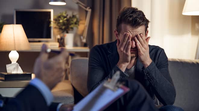 Wer kann mir durch die Krise helfen? Ein Psychotherapeut im Gespräch mit seinem Patienten, der das Gesicht in den Händen vergräbt.