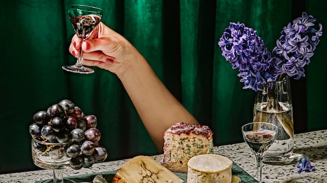 Ein Plädoyer für mehr Genuss Zuprostender Arm und üppig mit Lebensmitteln bestückter Tisch