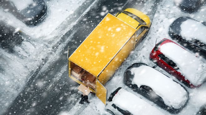 Das lange Warten aufs Geschenk Ein gelber Lieferwagen steht auf einem verschneiten Parkplatz zwischen anderen Autos.