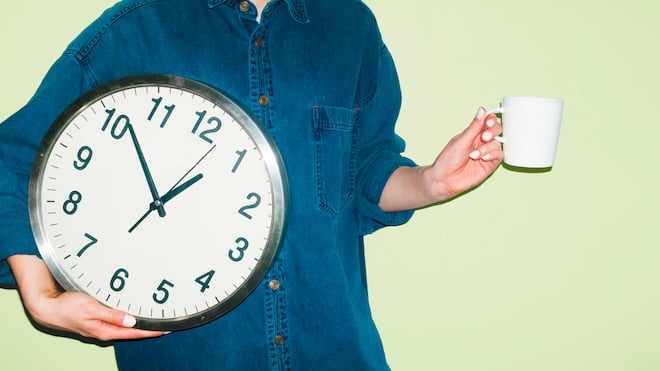 Ausstempeln zum Rauchen? Das muss sein – eigentlich Eine Person mit Kaffeetasse in einer Hand und einer Wanduhr in der anderen Hand vor grünem Hintergrund. Wie Arbeitspausen in der Schweiz geregelt sind, legt das Arbeitsgesetz klar fest.