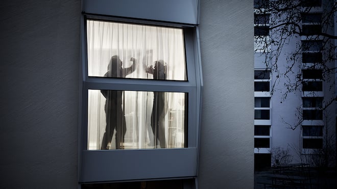 Wann schreitet die Polizei ein? Durch ein Fenster mit Vorhängen sieht man die verschwommenen Konturen eines sich streitenden Paares. Der Mann erhebt seine Hand und will offensichtlich zum Schlag ausholen, während sich die Frau mit den Armen zu schützen versucht.