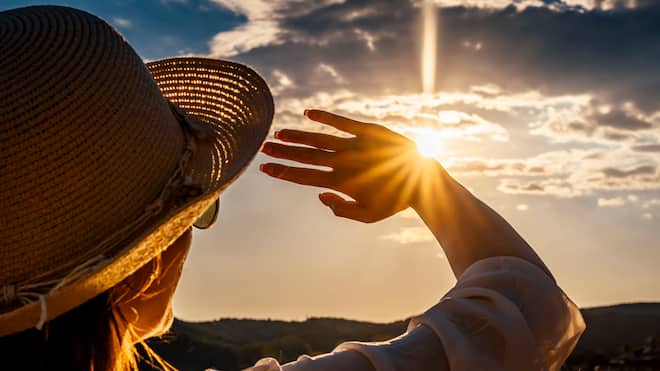 Hautfeind Sonne Eine Frau mit Sonnenhut und Sonnenbrille hält sich schützend die Hand vors Gesicht, um nicht von der Sonne geblendet zu werden