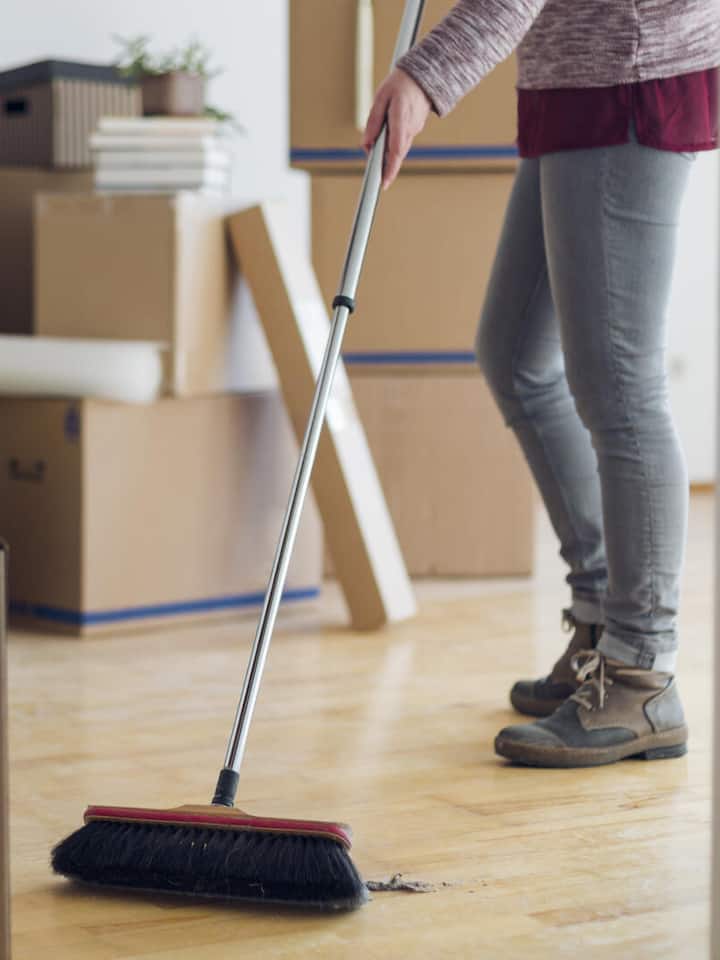 Eine Frau wischt den Boden einer Wohnung, im Hintergrund Umzugsschachteln.