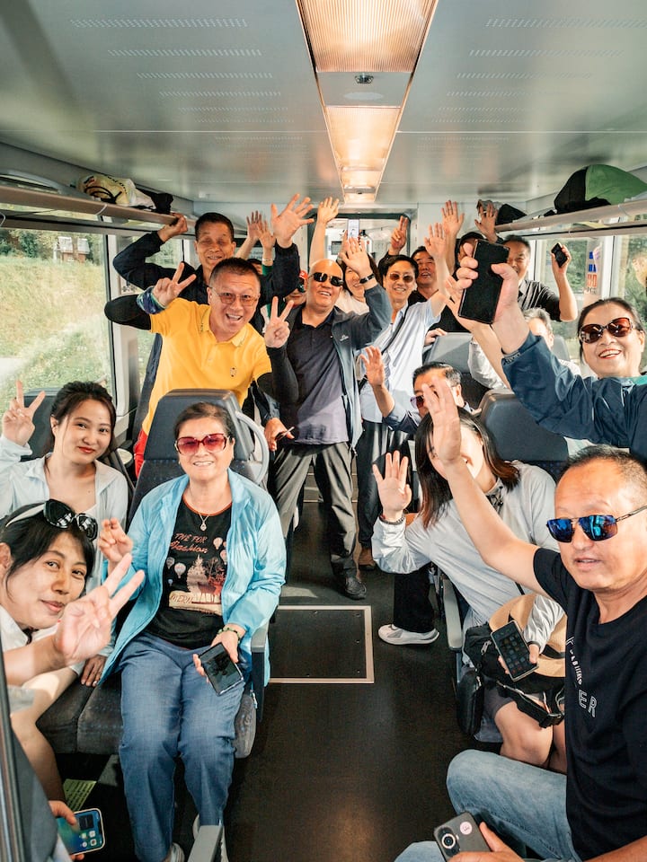 Chinesische Reisegruppe posiert lachend Zug - Die Schweiz leidet unter zu vielen Touristen, heisst es. Stimmt das? Eine Reise im sehr beliebten Panoramawagen von Luzern nach Interlaken