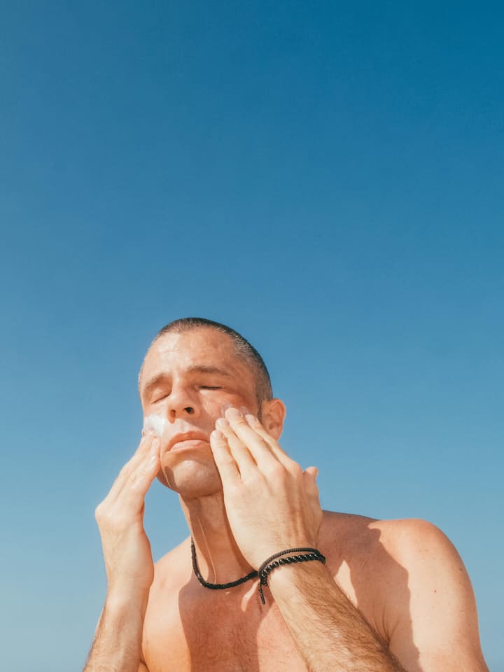 Günstigste Sonnencreme schlägt im Test teure Marken Man applying sunscreen to face against blue sky copy space, outdoor skincare and sun protection Florida Gulf Coast.