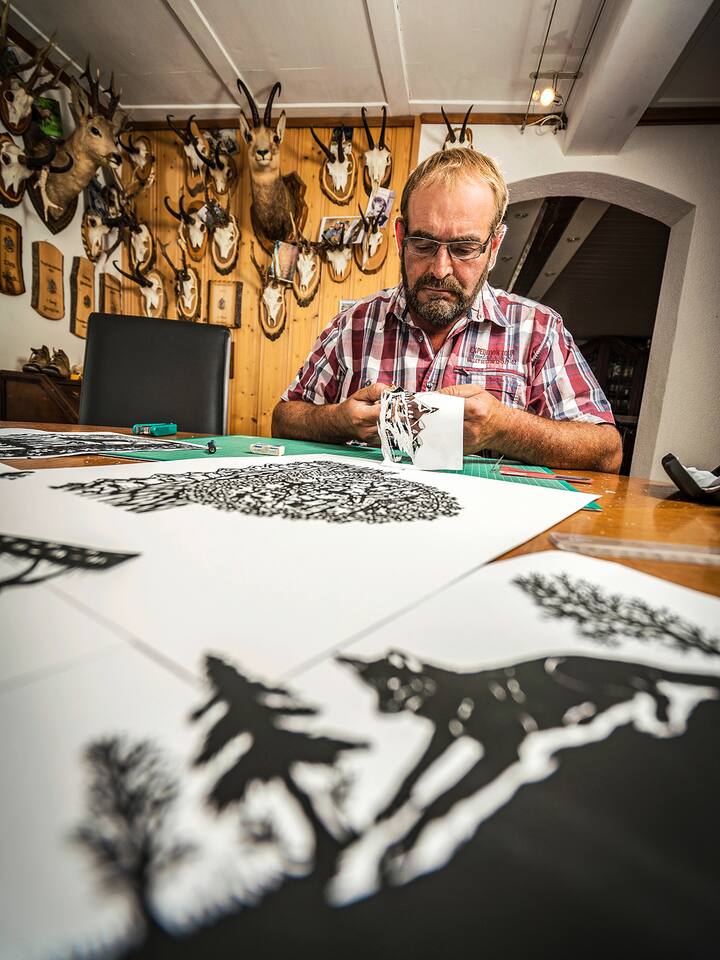 Paul Waser fertigt an seinem Stubentisch einen Scherenschnitt an